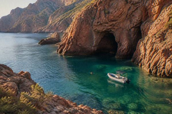 Boat below red cliffs of the Scandola coast