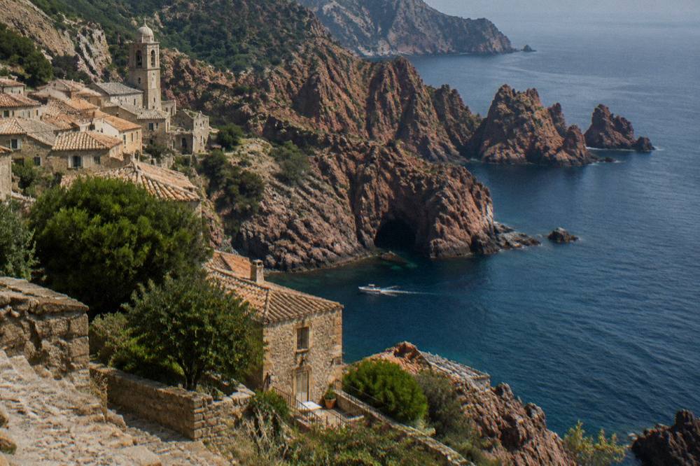 A small boat passing close to the red rock walls and a sea cave near Piana in Corsica