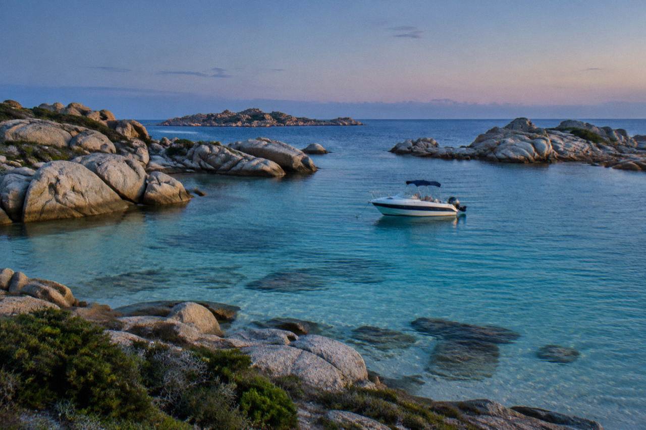 A boat anchored in a clear shallow bay between granite rocks at the Lavezzi islands