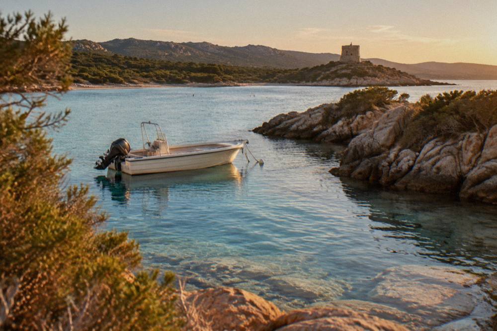 A small boat anchored in a narrow rocky inlet on the Corsican coast, with clear water over pale stone