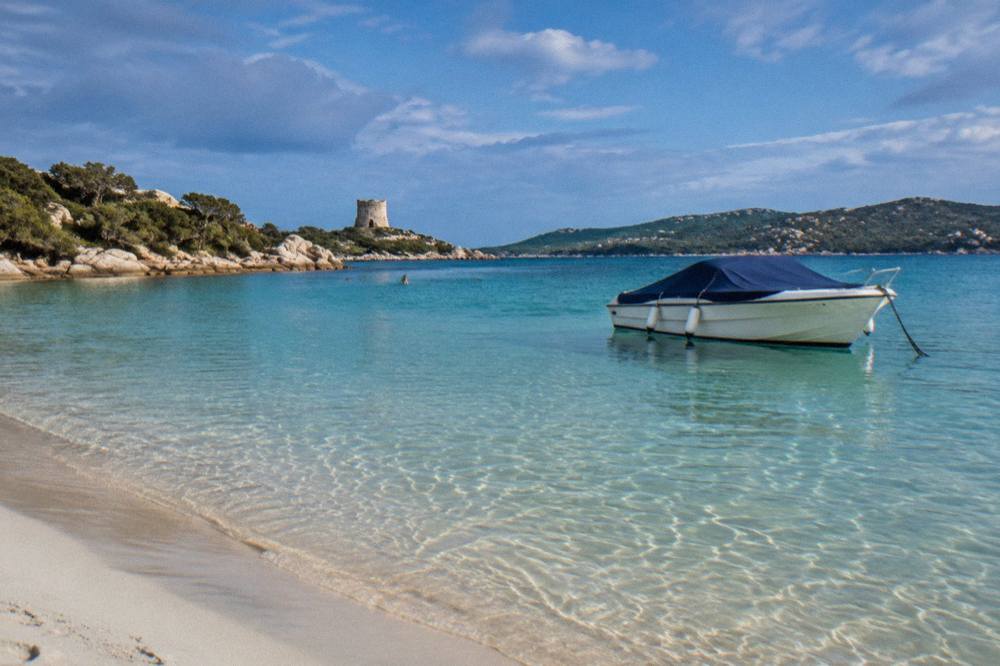 A covered boat anchored in a small Corsican harbour under a clearing sky after rain