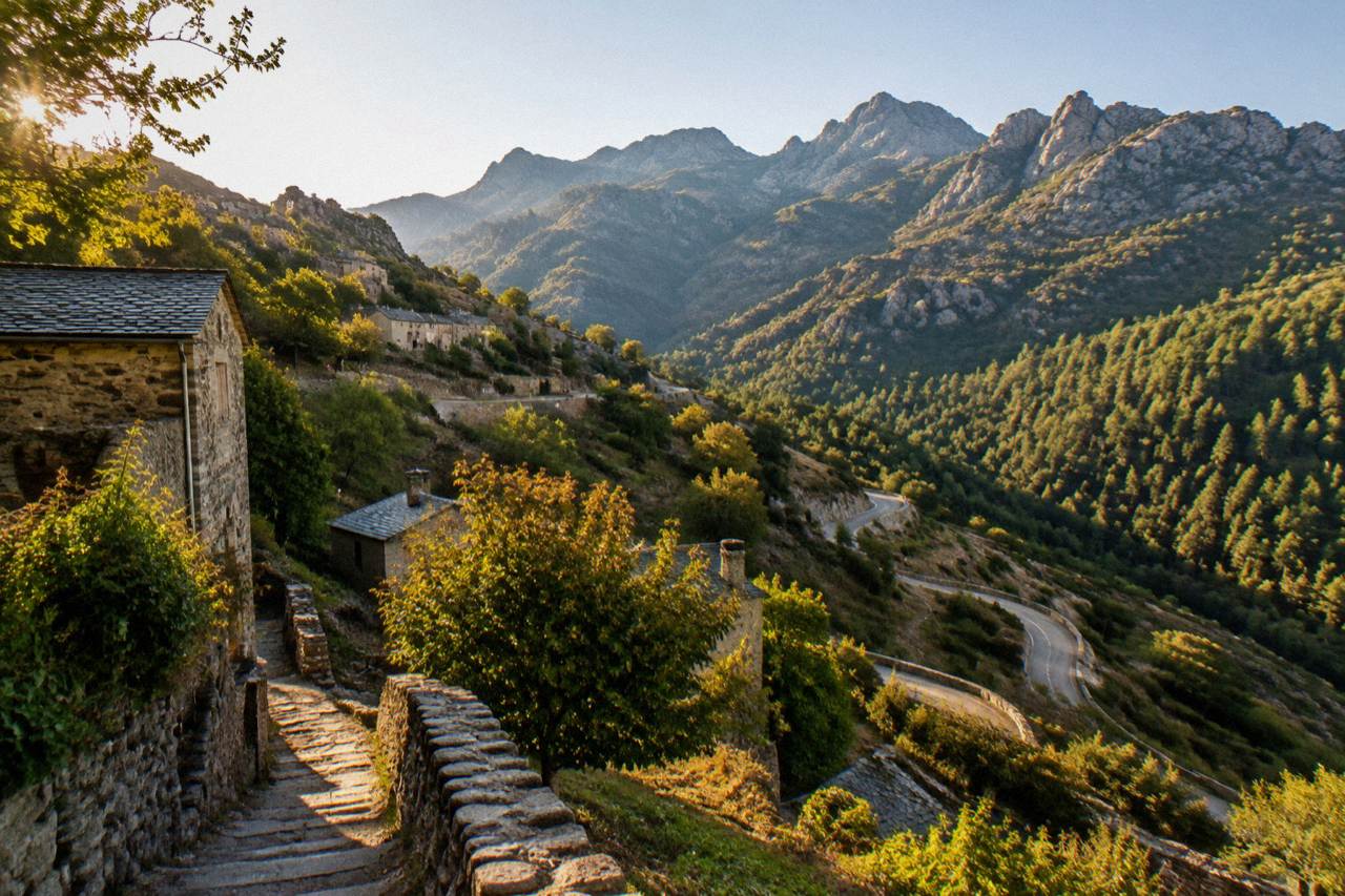 A winding mountain road with hairpin bends climbing through Corsican scrub toward high peaks