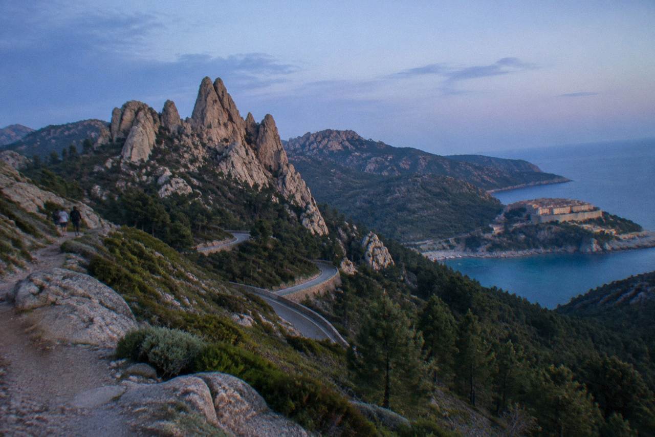 A stone citadel above a harbour with turquoise water and wooded hills in Corsica