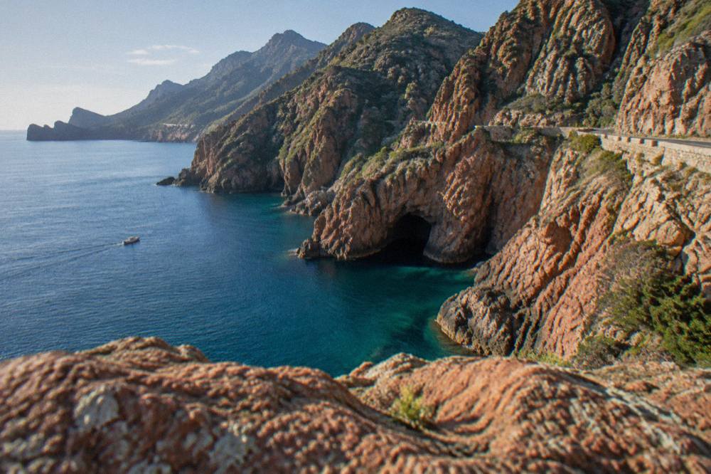 Red granite rock formations rising above the sea along a Corsian coastal road