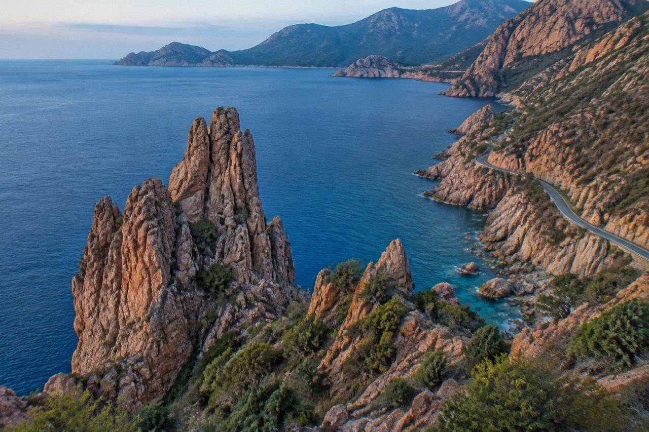 A rocky Corsican headland above clear sea with hills in the distance