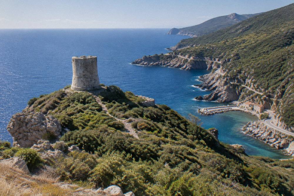 A small stone watchtower on a green headland above the Mediterranean