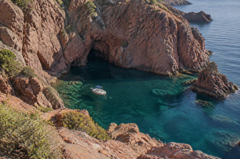 A small boat moored in a calm cove with red granite cliffs in Corsica