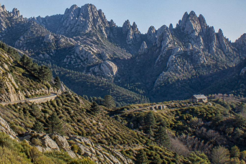 A granite mountain ridge above a Corsican valley with a stone refuge hut in the distance