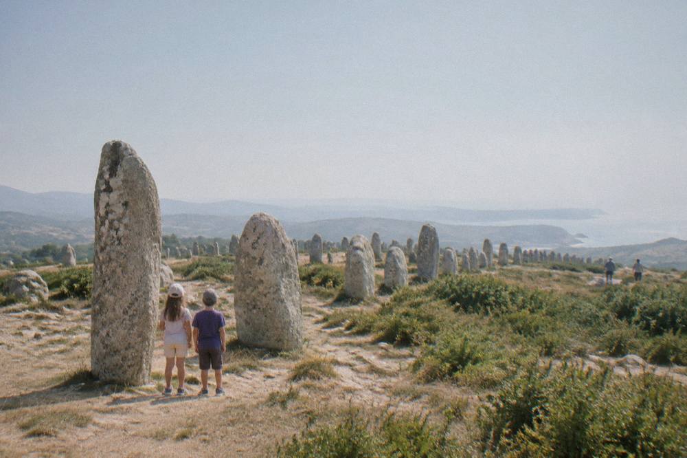 Children looking at ancient stone menhir statues at an open-air prehistoric site in Corsica