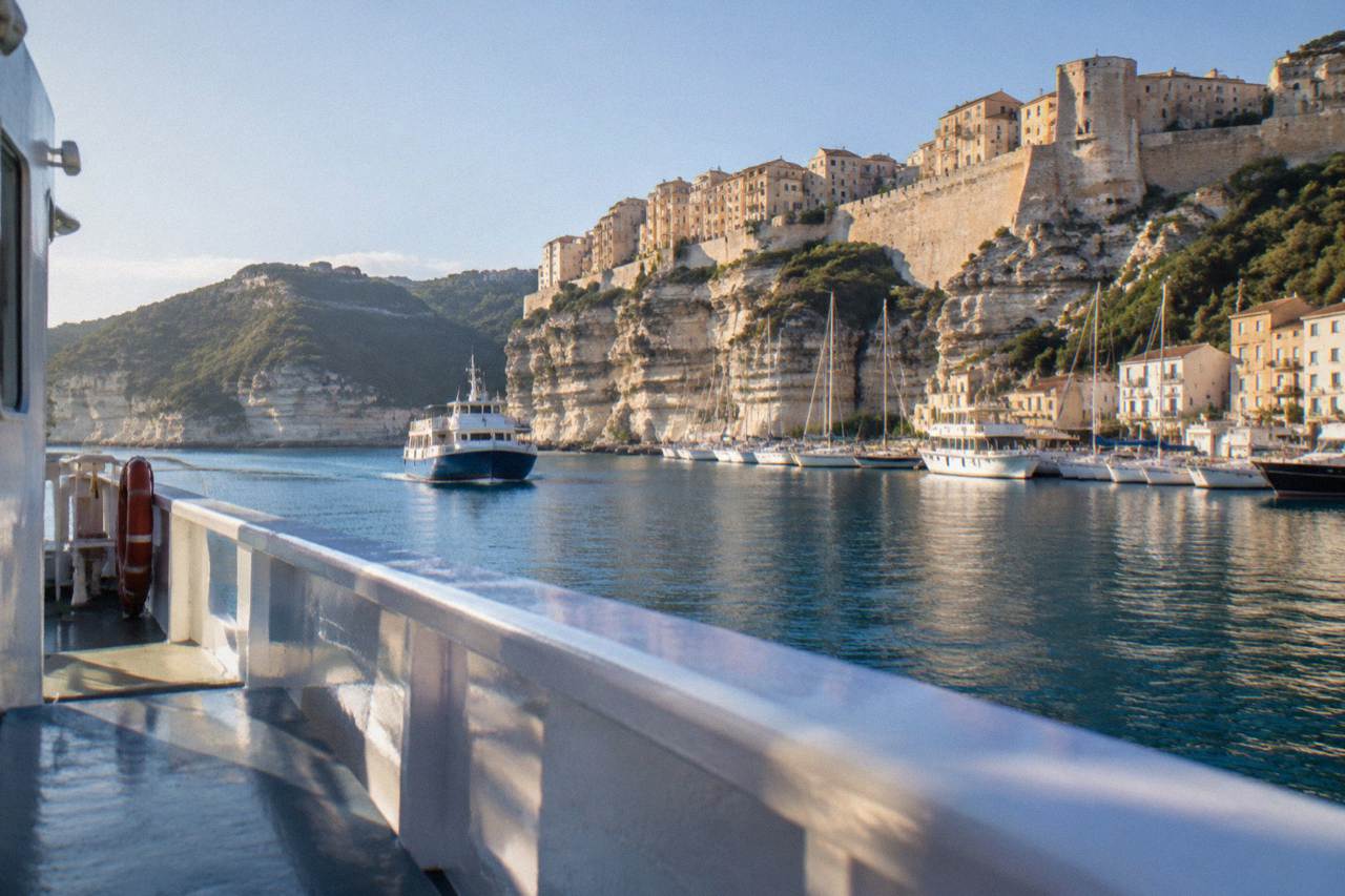 A ferry approaching a Corsican harbour town with hills rising behind the waterfront