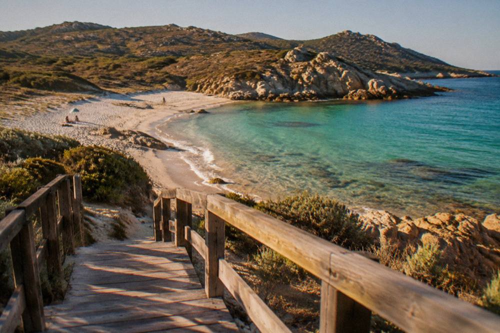 A wooden walkway leading down to a small cove with clear water in Corsica