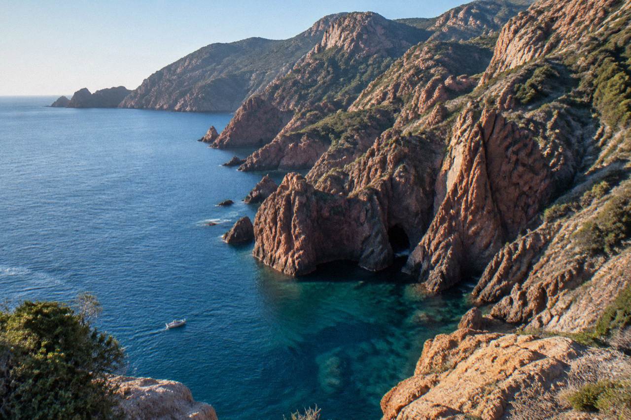 A Mediterranean coastline of red granite cliffs above clear sea on the island of Corsica