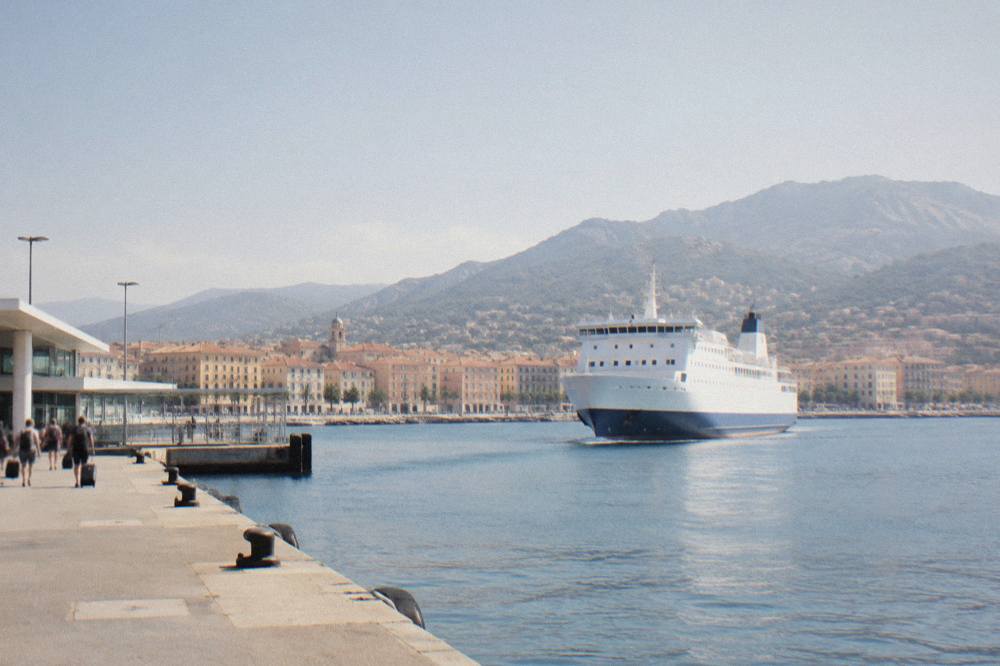 A ferry approaching a Corsican harbour town with hills rising behind the port