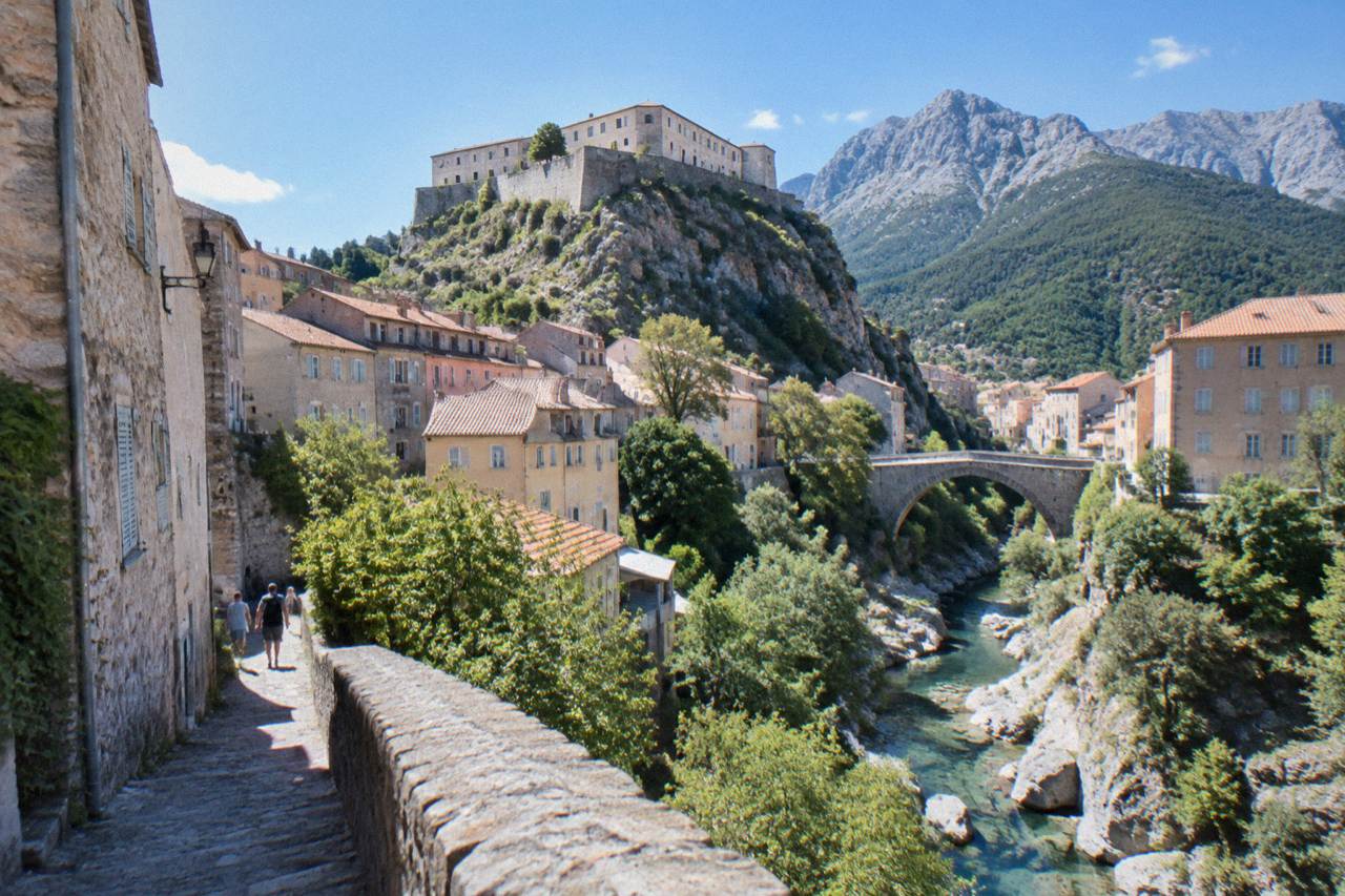 Stone buildings of a mountain town rising above a river gorge under a blue sky