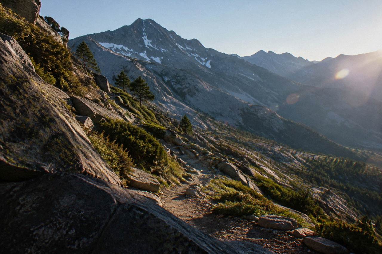 A rocky mountain path winding across high granite slopes with the Corsican mountains stretching into the distance