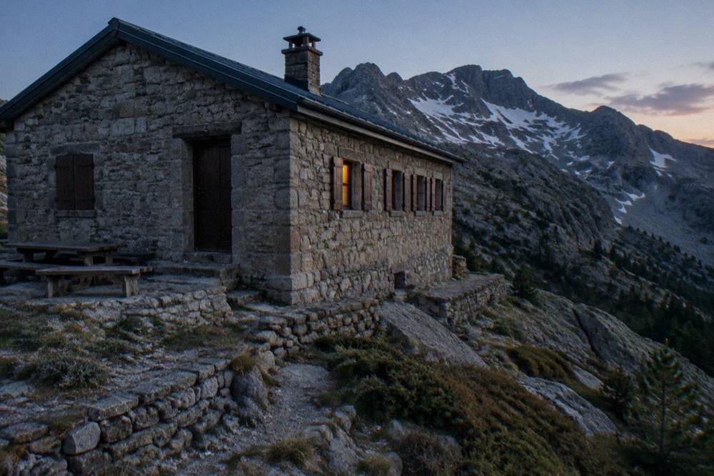 A stone refuge building on a mountain ridge above rocky slopes in the Corsican interior