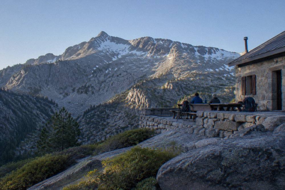 A mountain refuge hut above a granite landscape with hikers resting on the terrace