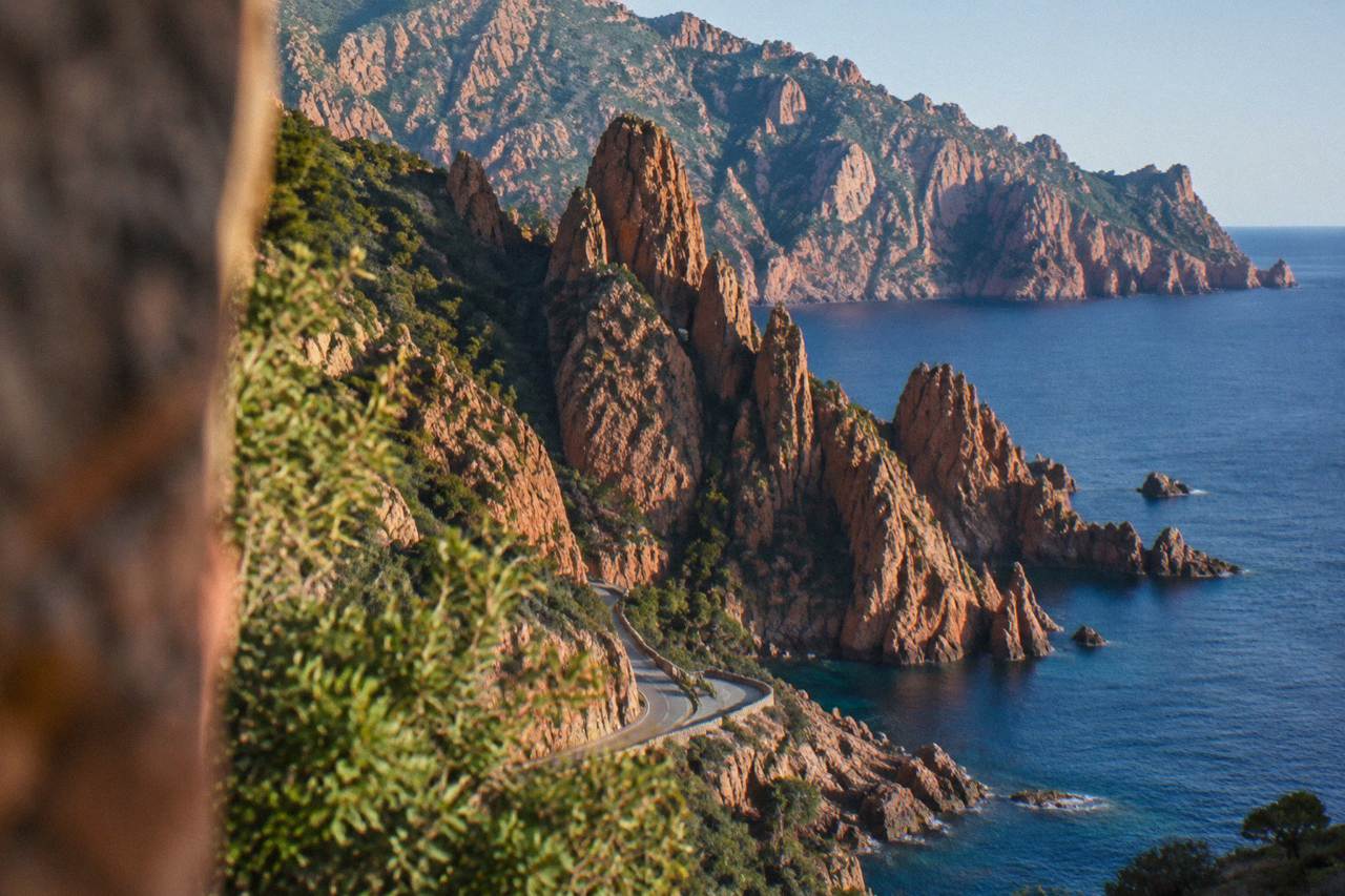 Red granite cliffs rising above clear water along the Calanques de Piana in Corsica
