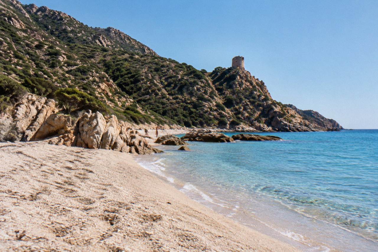 A curving Corsican beach of pale sand between granite rocks and clear shallow sea