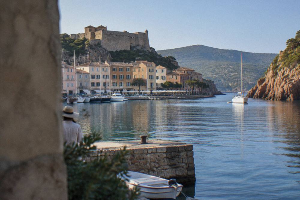 A white boat anchored in a narrow inlet between red granite cliffs on the Corsican coast