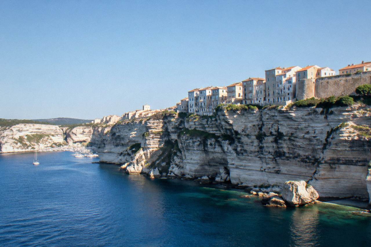 The citadel town of Bonifacio seen from the sea, white buildings standing on tall limestone cliffs above clear water