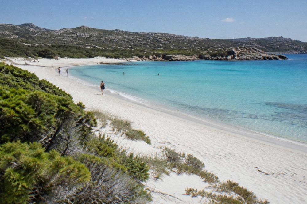 Turquoise water over sand at a sheltered Corsican cove with rocks at either end
