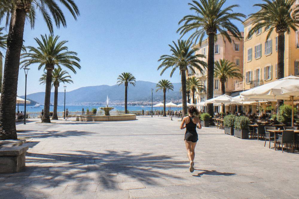 A quiet palm-lined square with pale facades and cafe terraces in the old centre of a Mediterranean port town