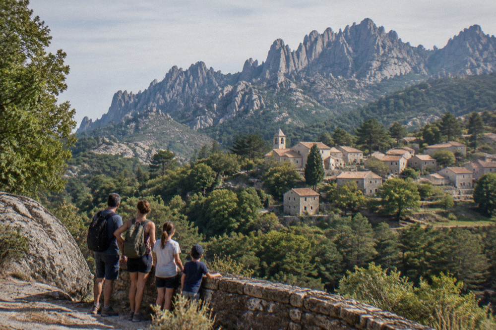 A family of visitors standing at a viewpoint above a forested valley in southern Corsica