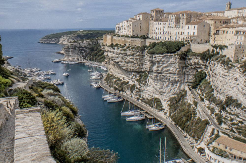 A narrow harbour below a clifftop walled town with moored sailboats