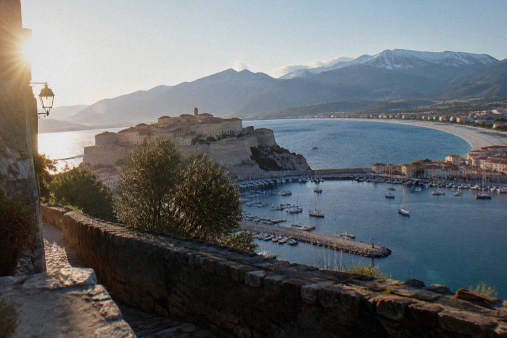 A hilltop citadel above a curved bay with a long beach and distant mountains