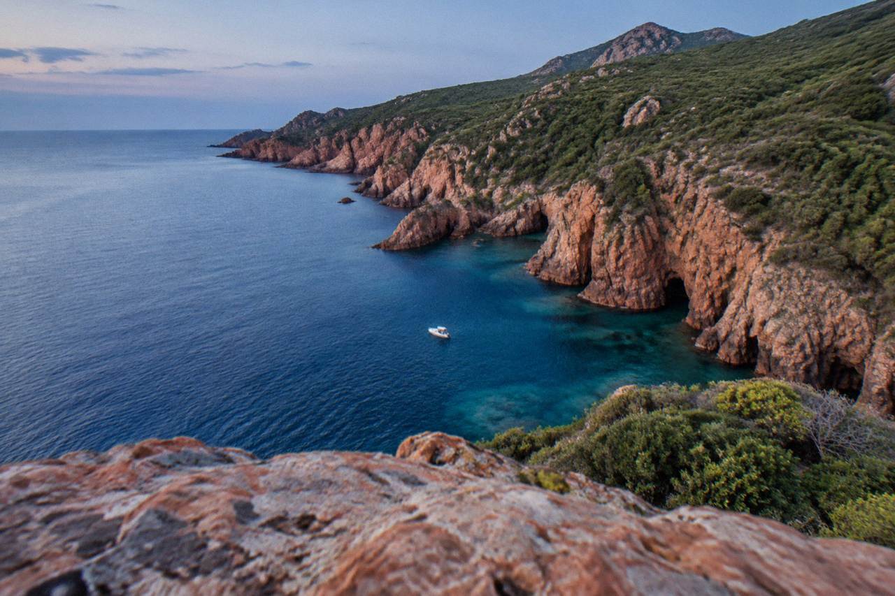 Aerial view of turquoise sea meeting red granite cliffs and green maquis hills on the Corsican coastline
