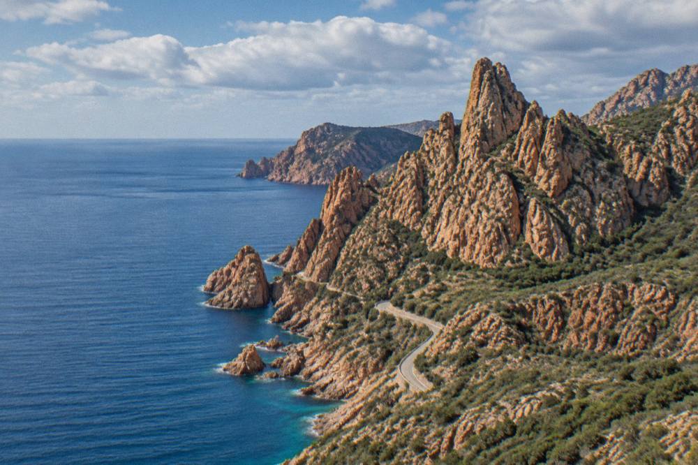 Red granite rock formations of the Calanques de Piana rising above calm blue sea