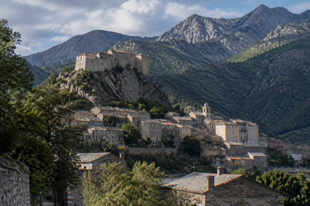 Stone houses of Corte beneath its citadel with pine-covered mountains behind