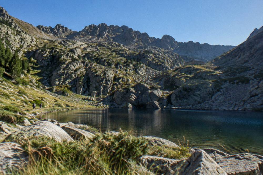 Mountain ridgeline trail with a stone refuge hut under a blue sky in central Corsica