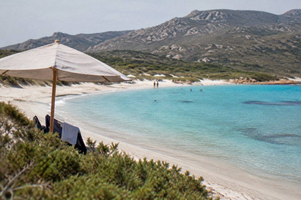 Wide sandy beach with shallow turquoise water and a few parasols in southern Corsica