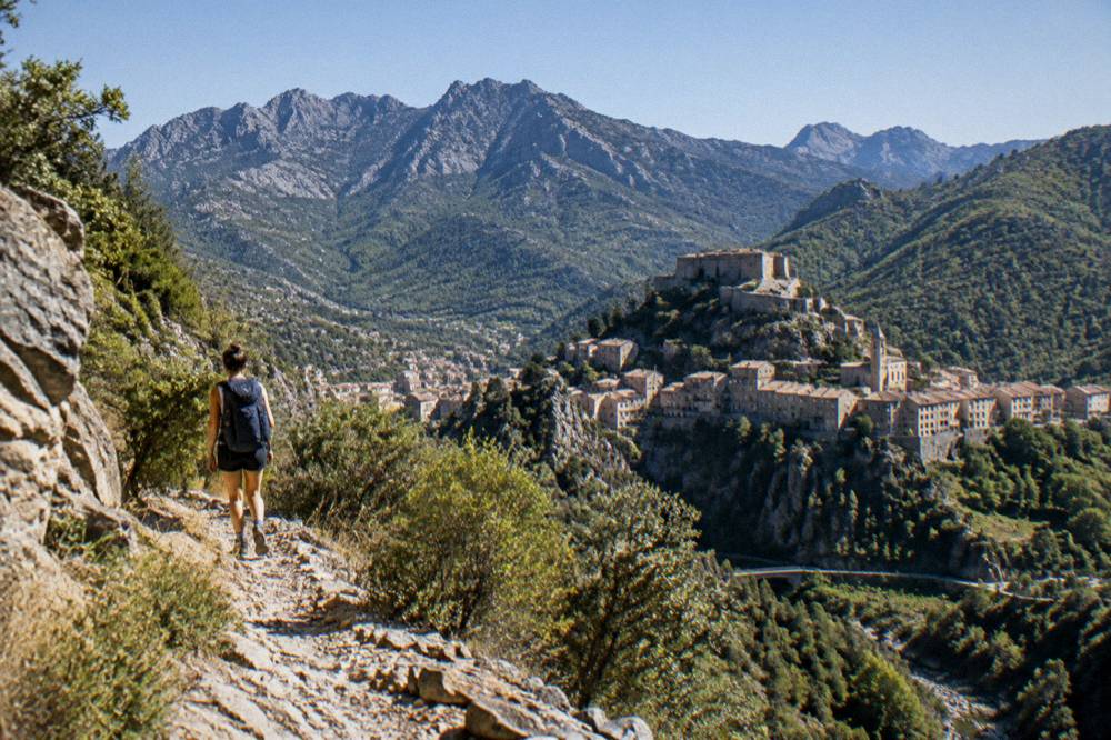 A walker with a backpack on a stony mountain trail above a deep valley