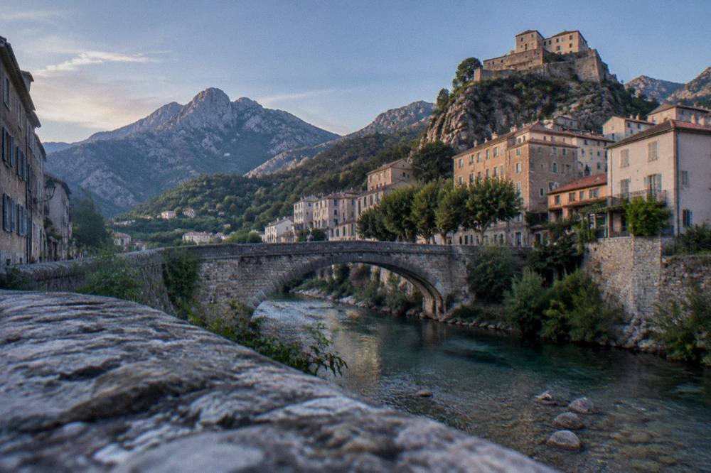 A stone bridge over a clear river with a historic town behind it