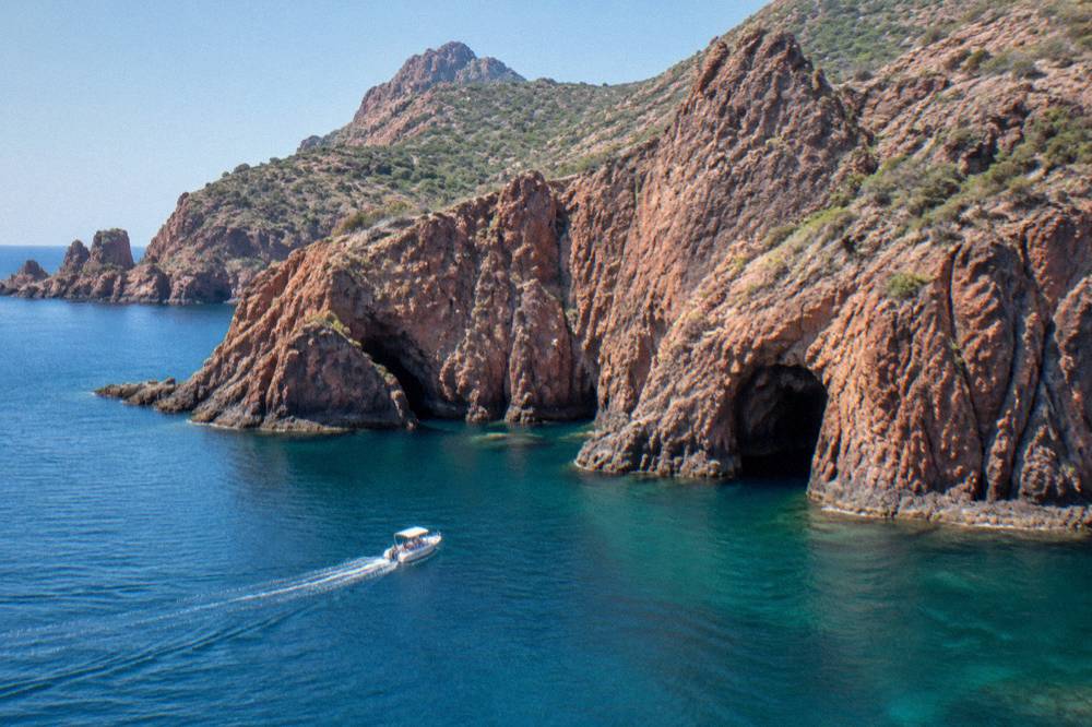 A boat entering the red rock sea cliffs of the Scandola reserve near the Gulf of Porto