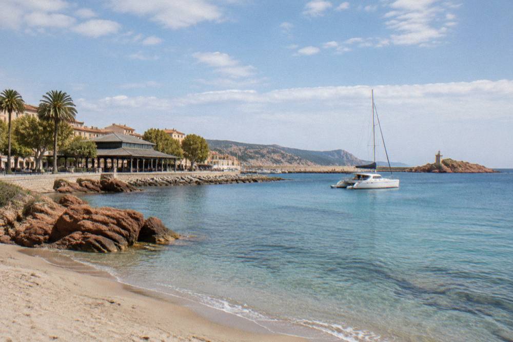 A catamaran anchored close to a sandy beach in a quiet Mediterranean cove
