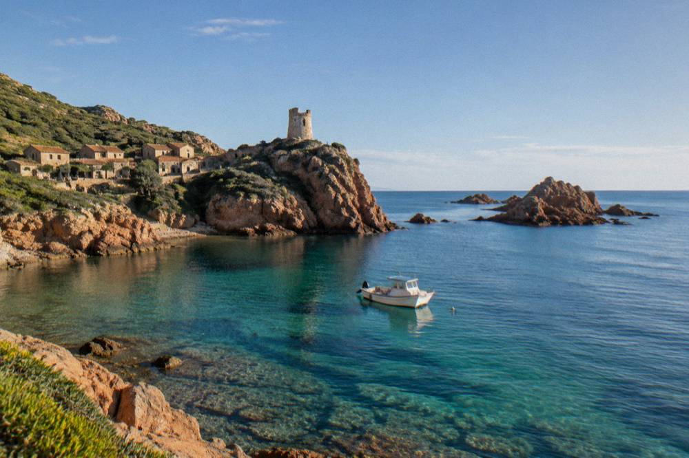 A small boat anchored above clear water near rocky islets off the south coast of Corsica