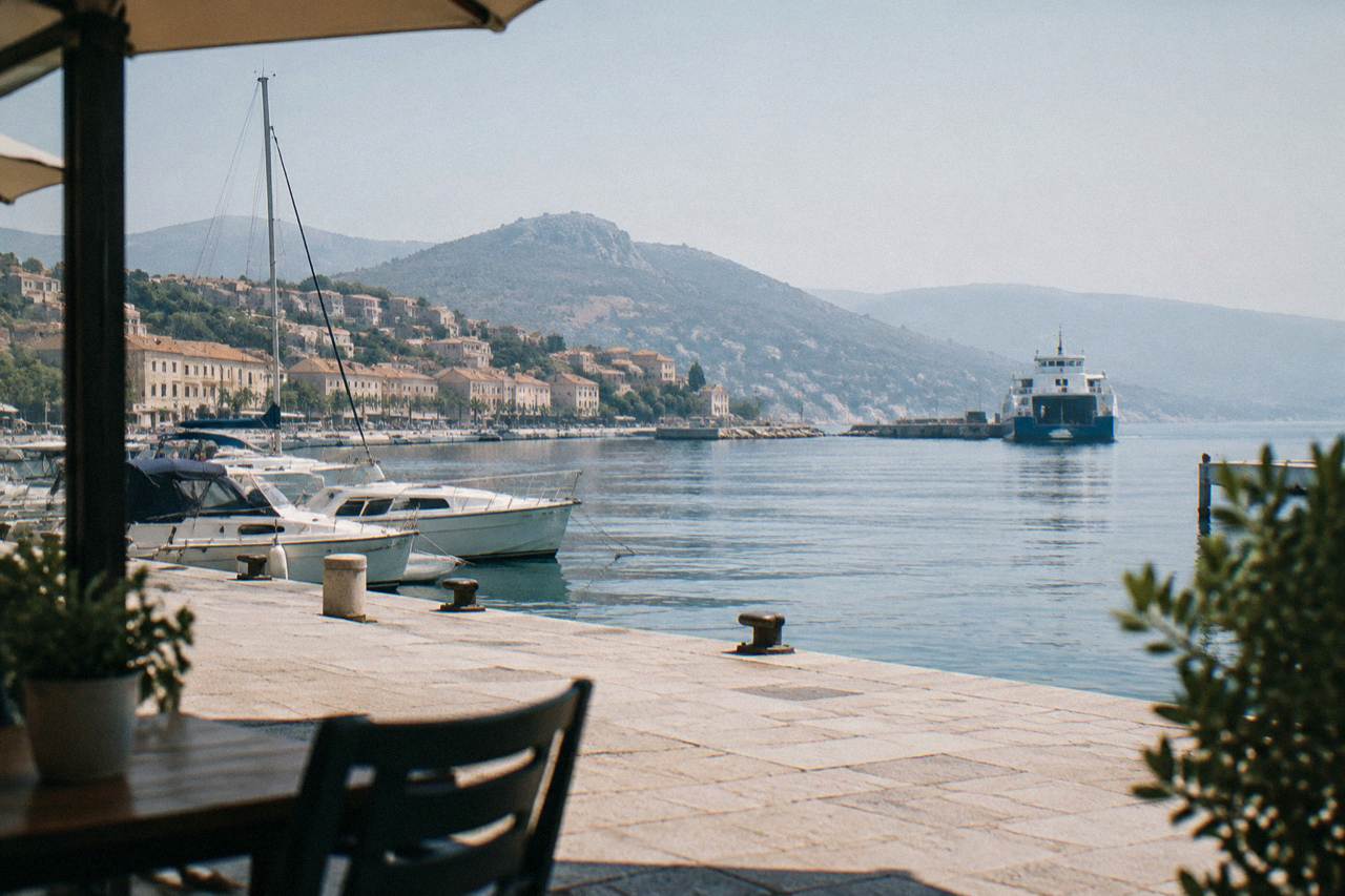 A small Corsican harbour town with boats moored along the quay and hills rising behind the buildings