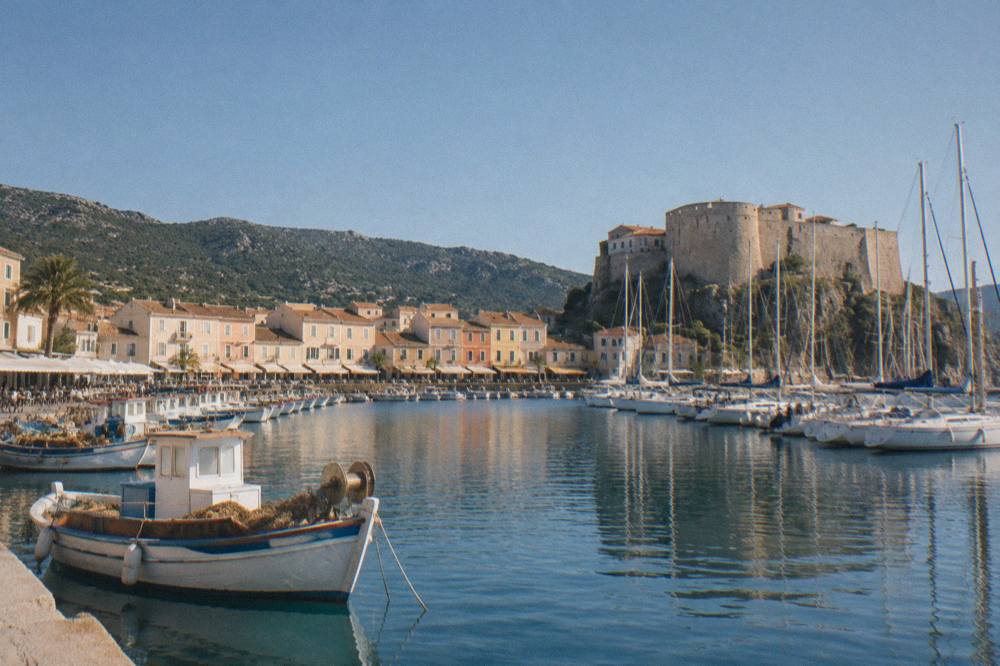 Fishing boats and moored sailing yachts in a sheltered Corsican marina at midday
