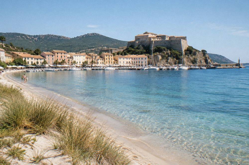 A white sand beach with dune grass and clear shallow water along an unspoilt Mediterranean shoreline
