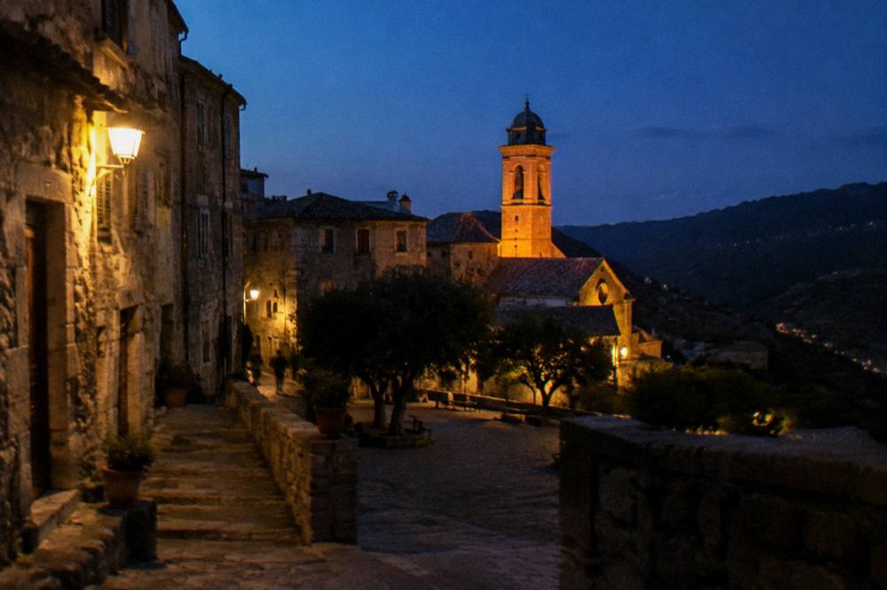 A granite hill town at dusk with warm light on stone walls and a church tower