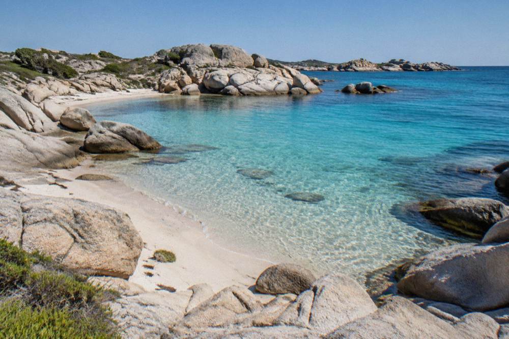Granite rocks and small coves on a low island with moored boats offshore