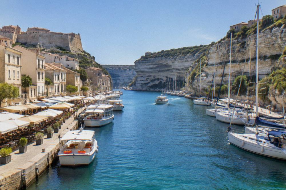 Fishing boats and small tour boats moored in a narrow harbour below steep town walls