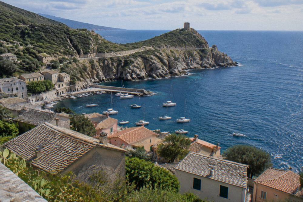 View over tiled rooftops of a Cap Corse village down to a sheltered inlet with moored boats
