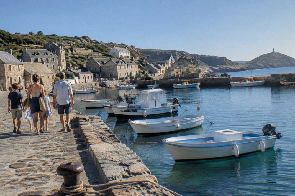 Family walking along a harbour wall past moored small boats in the late afternoon