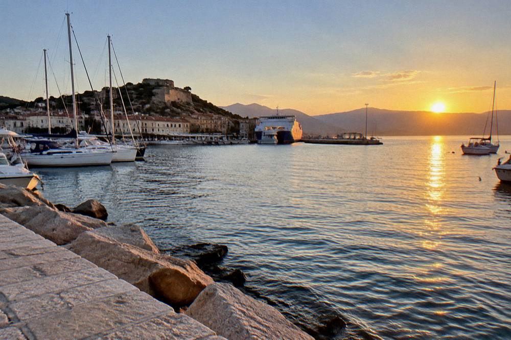 Sunset light over a small Corsican harbour with boats at rest and hills beyond