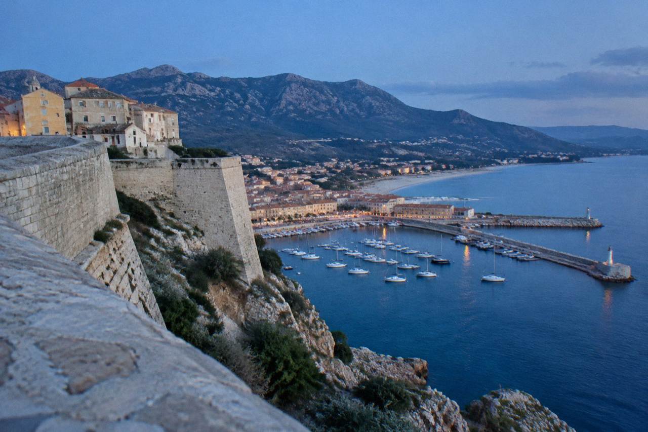 The stone ramparts of the Calvi Citadel against a blue sky above the Corsican coastal town